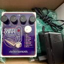 Bílý kytarový pedál s fialovým panelem a nápisem SYNTH /synthesizer machine. Na spodní části je logo electro-harmonix a seznam devíti presetů od 1 OB…