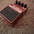 Kytarový efekt pedál v červeném kovovém provedení. Na horní části je nápis HOT ROD ROCK DISTORTION a čtyři ovládací knoflíky s popisky LEVEL, TONE, G…