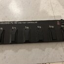 Černý MIDI kontrolér s nápisem BOSS FC-50 MIDI FOOT CONTROLLER. Zařízení má šest černých nožních spínačů, nad kterými jsou nápisy 1/6, 2/7, 3/8, 4/9,…