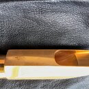 Detail zlatého mouthpiece nástroje z kovu, který leží na černé kůži. Na povrchu je vyryto logo složených písmen „SD“ a malý nápis „X 9“. Povrch je hl…