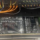 Fotografie zachycuje vnitřek černého rackového case s audio vybavením. V horní části jsou zapojené kabely různých barev (černé, oranžové, červené) do…