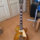 Zlatá elektrická kytara s tvarem singlecut a bílým pickguardem. Na hlavě je nápis „Stanley Brown“ a na hrazdnu viditelný nápis „Custom“. Kytara je um…