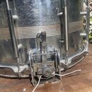 Detailní záběr na spodní část kovového bubnu v chromovaném provedení. Na povrchu jsou viditelné škrábance, otěrky a oxidace kovu. V dolní části je um…