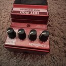 Červený kytarový efekt s nápisem HOT ROD ROCK DISTORTION a logem DigiTech. Na přední straně jsou čtyři černé otočné ovířky a nápisy X-SERIES, OUT 1 (…