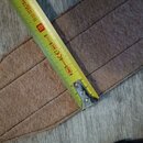 Detail hnědého plstěného popruhu s prošívanými segmenty. Přes popruh je položen žlutý skladovací metr, který ukazuje délku v centimetrech. Povrch mat…