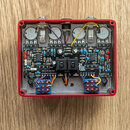 Interiér červeného efektového pedálu s viditelnými elektronickými komponenty na základní desce. Na desce je bílý nápis RedPrint a logo pedal pawn. Js…
