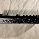 Černý hudební procesor značky LINE 6. Zadní strana zařízení obsahuje vstupní a výstupní konektory s nápisy PEDAL 2, GUITAR IN, FX RETURN (LEFT/MONO,…