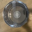 Průhledný buben s kovovým obručem, který obsahuje bílý tlumicí pás přes střed. Na povrchu je viditelné logo EVANS a nápis LEVEL 360. Nástroj leží na…