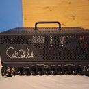 Černý kytarový zesilovač v perforovaném kovovém šasi s rukojetí. Na přední straně je bílý nápis Paul Reed Smith a červený nápis MT15. Ovládací panel…