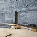 Tmavně hnědá elektrická kytara položená v otevřeném kufru s šedým plyšovým vnitřkem. Na kytaru jsou vidět struny, hradelník a černý most. Nástroj nem…