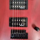 Detail červené elektrické kytary se dvěma černými humbuckery. Na obou snímačích je bílý nápis Jackson. Pod snímači je umístěn černý strunník. Povrch…