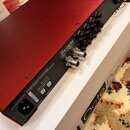 Zadní strana červeného audio rozhraní značky Focusrite (nápis Focusrite, pod ním menšími písmy Focusrite Audio Engineering Ltd). Jsou zde vidět konek…