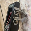 Černá hlava basové kytary s nápisem stagg. Na straně jsou umístěny dva kovové ladičky s vřeteny a klíči. Povrch nástroje je matný, kovové části vykaz…