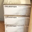 Stoh pěti bílých papírových krabic. Na každé krabici je černý nápis CELESTION a adresa www.celestion.com. Povrch krabic je doplněn šedým grafickým mo…