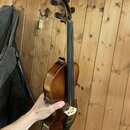 Dřevěné smyčcové nástroje, pravděpodobně housle, v hnědém lakovaném provedení. Nástroj je držen v ruce před dřevěnou stěnou. Na fotce nejsou žádné vi…