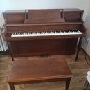 Hnědé dřevěné piano s doprovodnou stoličkou. Nad klávesnicí je vyveden nápis WILLIS. Povrch nástroje i stoličky vykazuje drobné známky opotřebení.