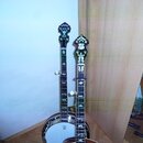 Dvě banjota s tmavým hřidlem a bílými ladicími kolíčky. Pravé banjoto má na hlavě nápis "KAY" v bílém rámovém logu a je zdobeno ornamenty. Hřidla obo…