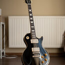 Černá elektrická kytara s jednovýstupním tělem a hnědým lemováním. Na hlavě je zlatý nápis Gibson. Kytara má dva humbuckery, čtyři otočné knoflíky a…