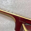 Detailní pohled na spoj hředne s tělem červené kytary. Je vidět světlá hmatnice a jedna natažená struna. V místě spoje je patrná mezera v laku a nesr…