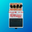 Stříbrný kytarový pedál s nápisem Bass Synthesizer SYB-3. Na horní straně jsou čtyři černé ovládací knoflíky a červená kontrolka CHECK. V dolní části…