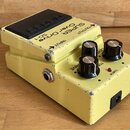 Žlutý kytarový efekt s černým spínacím pedálem. Na horní části je nápis SUPER Over Drive SD-1 a označení vstupů INPUT a OUTPUT. Efekt má tři černé ko…