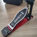 Červený bubnový pedál s kovovou stlačovací deskou a černým šlapákem. Na kovové části je vyryto „DW 5000“ a nápis „The Drummer's Choice.®“. Na šlapáku…