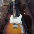Elektrická kytara s tělem v barvě sunburst a bílým pickguardem, položená na černém obalu. Na hlavě hředu je viditelné logo "Ltd". Nástroj vykazuje zn…