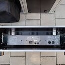 Zadní strana černého elektronického zařízení umístěná v transportním kufru. Na zadním panelu jsou vidět konektory, vypínač a nápisy včetně log CE a U…