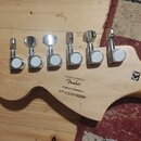Zadní strana hlavy kytary z přírodního dřeva s šesti chromovanými ladičkami s bílými knoflíky. Na dřevě je černý nápis: Designed and Backed by Fender…