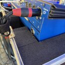 Modrý elektronický přístroj s kovovým horním panelem, do kterého je zapojen kabel s červeným konektorem v portu označeném nápisem AUDIO IN. Na přístr…