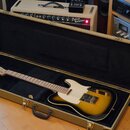 Elektrická kytara s tónem sunburst v hnědo-žlutých odstínech, uložená v otevřeném tvrdém kufru s černým vnitřkem. Kytara má světlý hриф a bílý pickgu…