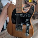 Elektrická kytara s tělem z dřeva s viditelnou masivní strukturou a hnědým lakem. Černý pickguard obsahuje bílý grafický přítisk s podobou postavy. N…
