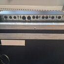 Stříbrný rackový přístroj umístěný v transportním kufru. Na zadním panelu jsou viditelné konektory a nápisy: HEAD PHONE, MIDI (THRU/OUT), OUTPUT (SEN…