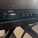 Zadní panel černého hudebního přístroje značky KORG. Je zde uveden nápis MODEL, SERIAL NO. 321829 a AC V 50/60Hz W, dále KEIO ELECTRONIC LABORATORY C…