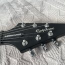 Černá hlava elektrické kytary s nápisem Epiphone v bílém skriptovním písmu. Na hraně hředu je viditelný nápis ANNIHILATION. Nástroj má chromované lad…