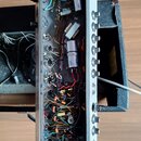 Fotografie zachycuje vnitřek elektronického zařízení s otevřeným šasi, které obsahuje množství kabelů, kondenzátorů a jiných komponentů. Na pravé str…