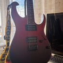 Elektrická kytara s červeným gradientem do černé, vybavená dvěma humbuckery a fixním mostem. Na kytaru je nasazen žlutý popruh s nápisem CROSS. Povrc…