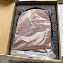 V kartonové krabici s černou pěnovou vložkou je uložen hnědý dřevěný nástroj zabalený v průhledné plastové fólii. Na povrchu je vyryt nápis PORTEGA®…