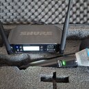 Černý bezdrátový mikrofonní systém značky SHURE v přepravním kufru s pěnovou výplní. Přijímač má na horní straně nápis SHURE a v čele displej s ovlád…