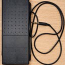 Černý sustain pedál s protiskluzovou gumovou texturou a nápisem YAMAHA. K pedálu je připojen černý kabel s 6,3mm jack konektorem. Povrch pedálu vykaz…