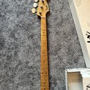 Hrabedlo basové kytary s přírodním dřevěným povrchem a hmatníkem z jasného dřeva. Na hlavě je viditelné logo Fender a nápis Jazz Bass. Nástroj vykazu…