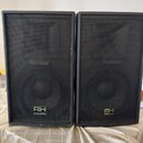 Dvě černé reproduktorové bedny s kovovými mřížkami. Na spodní části obou beden je umístěn nápis RH SOUND. Povrch beden vykazuje mírné opotřebení hran.