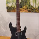 Černá elektrická kytara s matným povrchem a hnědým hmatníkem. Na hlavě je bílý nápis Ibanez. Nástroj má dva humbuckery, chromovaný most a jeden ovlád…