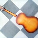Zadní strana akustické kytary s hnědým gradientním lakem (sunburst). Nástroj má dřevěný krk a hlavu s bílými ladičkami. Na povrchu těla jsou viditeln…