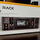 Fotografie zobrazuje digitální mixážní pult v rackovém provedení, umístěný před svým původním obalem. Na přístroji je viditelné logo behringer a nápi…