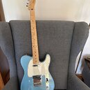 Modrá elektrická kytara s jasným javorovým hnedkem a bílým pickguardem. Na hlavě je viditelné logo Fender. Kytara má jeden snímač u mostu a jeden v k…