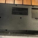 Fotografie zachycuje spodní stranu černého elektronického nástroje. Na štítku je uveden výrobce Roland Corporation, nápis MADE IN MALAYSIA a několik…