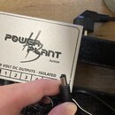 Stříbrný kovový napájecí adaptér s nápisem POWER PLANT Junior a textem 9 VOLT DC OUTPUTS - ISOLATED. Na spodní straně jsou viditelná čísla 1, 2 a 3 v…