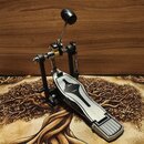 Kovový pedál basového bubnu v stříbrné a černé barvě. Na plošince je vyfrézovaný černý ornament ve tvaru stylizované lahve nebo kapky. Nástroj vykazu…