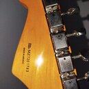 Zadní strana hlavy kytary z dřeva s viditnou masou. Na povrchu je černý nápis MADE IN MEXICO a SERIAL NUMBER MZ7201763. Vpravo jsou umístěny šest chr…
